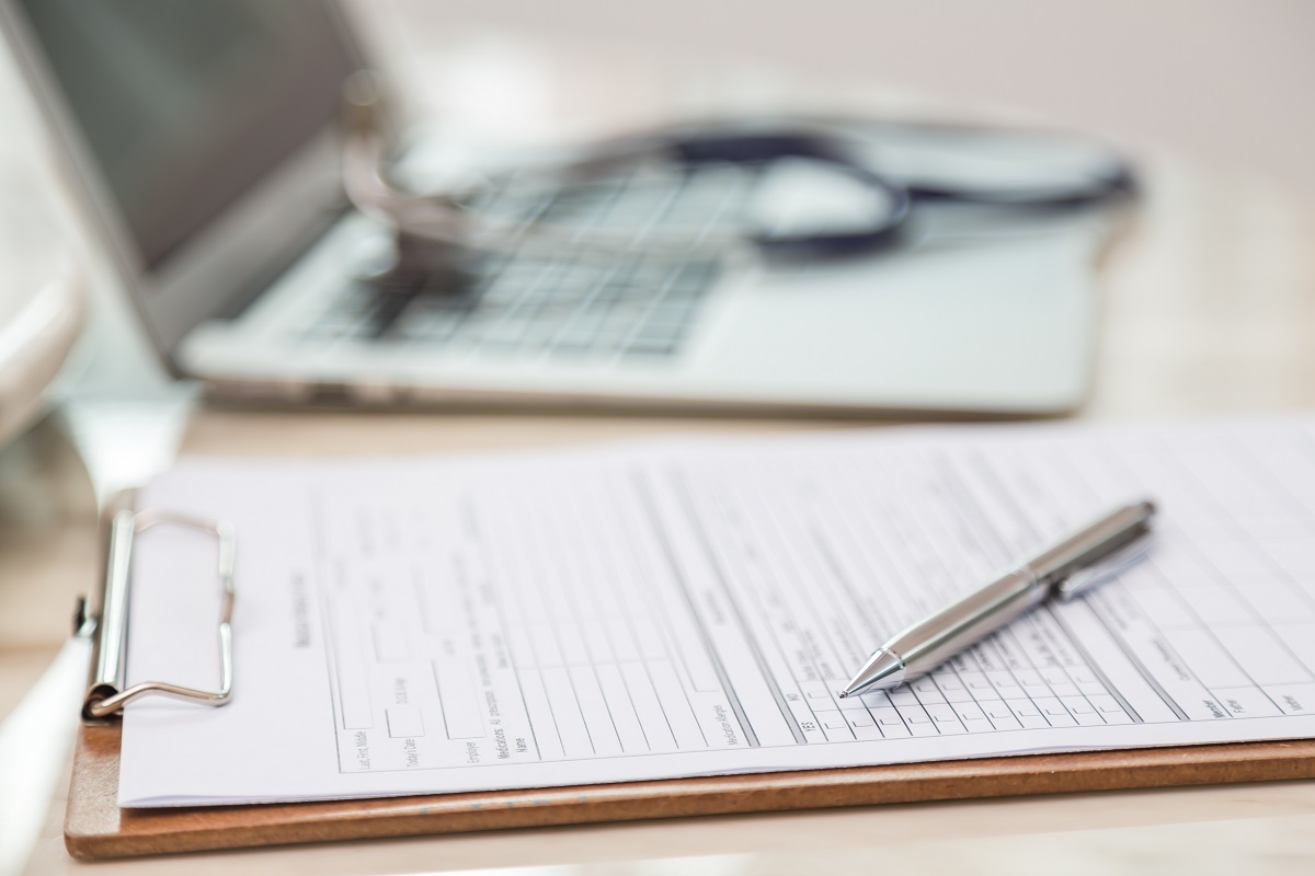 Notepad, pen and clipboard with a computer in the background